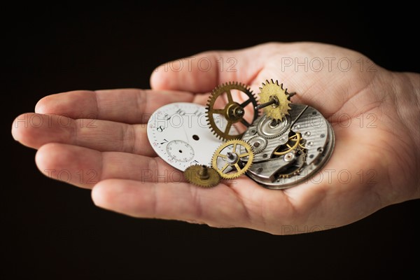 Close up of hand holding clock parts.