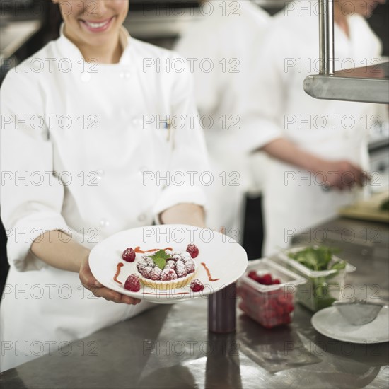 Chefs preparing food in kitchen, women showing dessert.