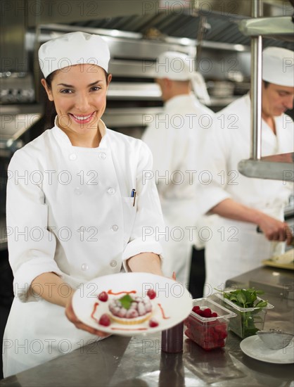 Chefs preparing food in kitchen, women showing dessert.