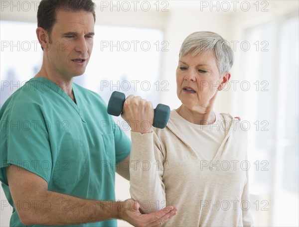 Man assisting  senior woman in weight lifting.