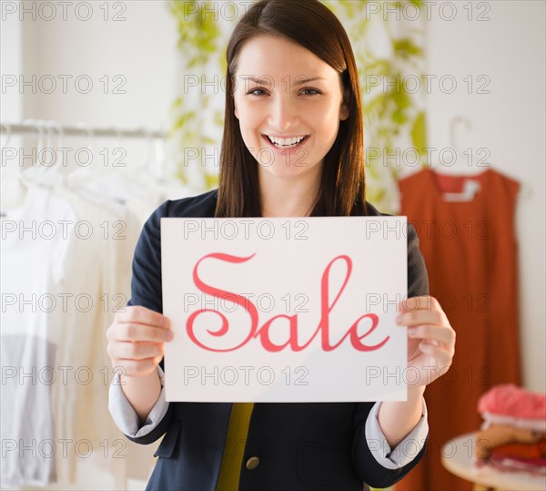 Young woman holding "sale" sign. Photo : Jamie Grill Photography