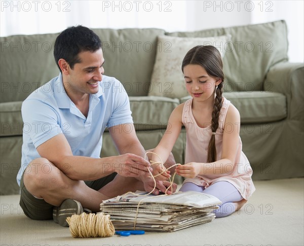 Father and daughter (8-9) wrapping up wastepaper bundle.