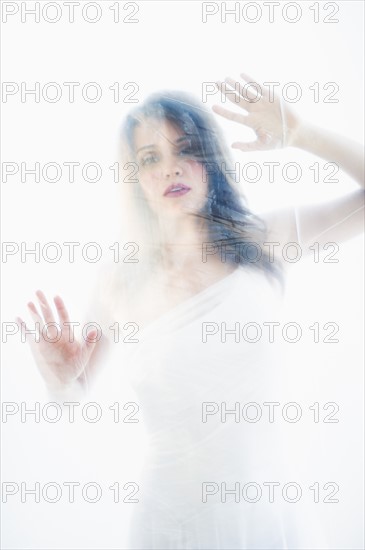 Young attractive woman looking from behind white sheet.