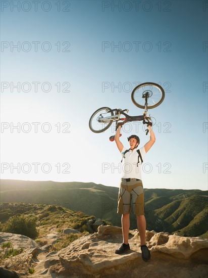 USA, California, Laguna Beach, Mountain biker on top of hill holding up his bike.