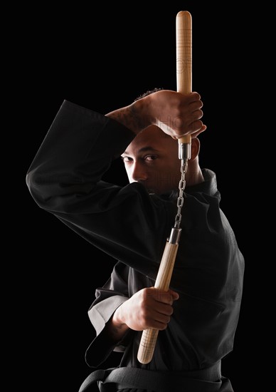 Studio shot of man exercising with nunchaku . Photo : Mike Kemp