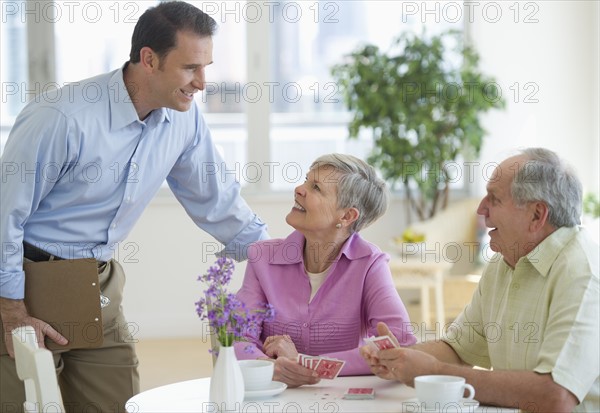 Smiling man talking to senior couple playing cards.