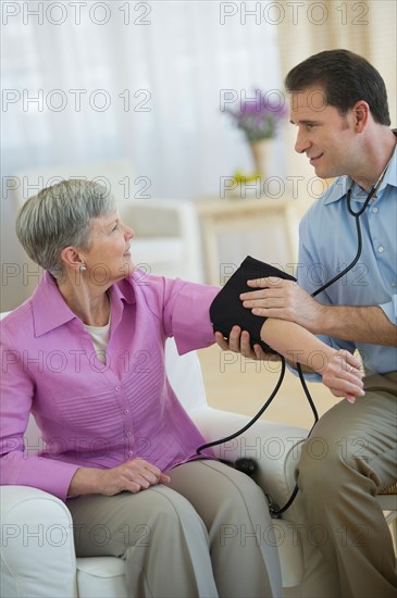 Smiling man taking senior woman's blood pressure.