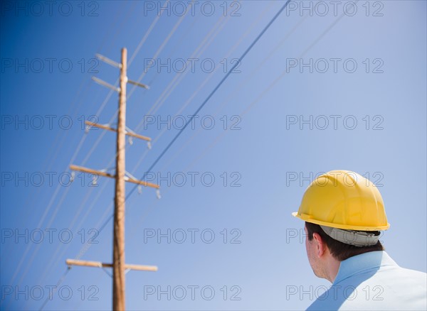 Man in hard hat looking at telephone pole. Photo : Jamie Grill Photography