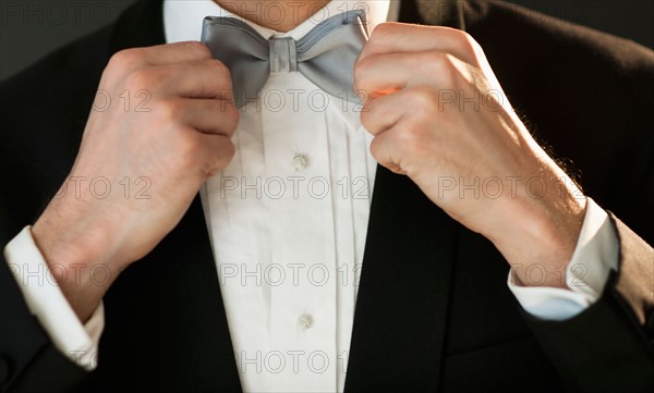 Studio shot of bridegroom adjusting bow tie.