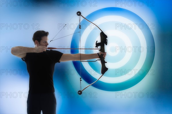 Man holding bow and aiming with blue circle in background.