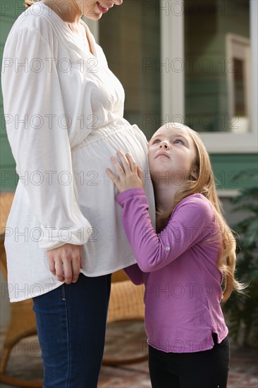 Girl (4-5) putting ear to expectant mother's belly. Photo : Rob Lewine