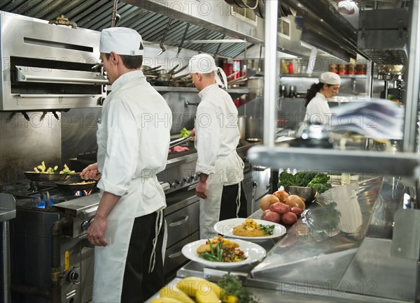 Chefs preparing food in kitchen.