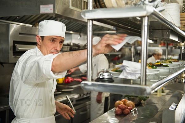 Chef putting order on stick, in background chefs preparing food.