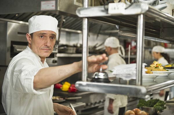 Chef ringing service bell, in background chefs preparing food.