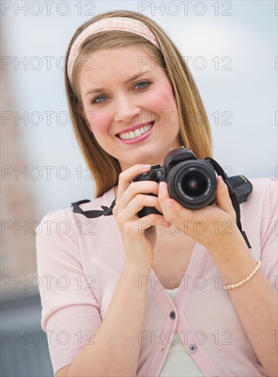 Portrait of young woman holding camera, smiling.