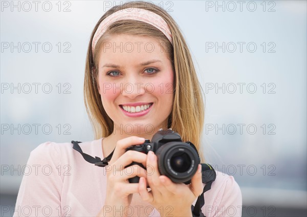 Portrait of young woman holding camera, smiling.