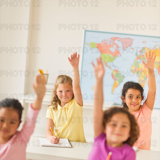 Four girls (6-9) raising hands in classroom.