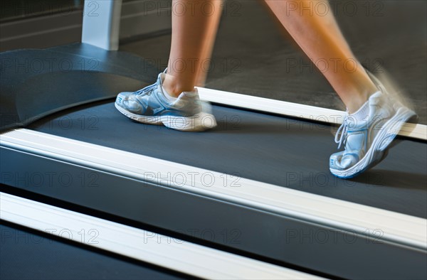 Low section of woman walking on treadmill.