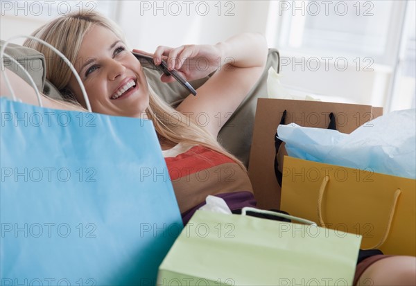 Young woman talking on mobile phone surrounded by shopping bags. Photo : Jamie Grill