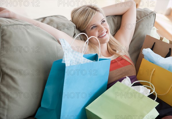 Young woman sitting on sofa surrounded by shopping bags. Photo : Jamie Grill