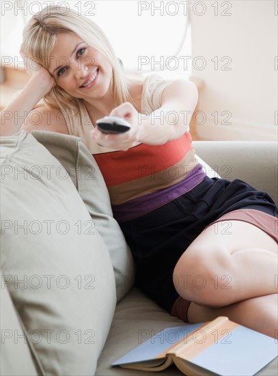 Young woman sitting on sofa with remote control. Photo : Jamie Grill