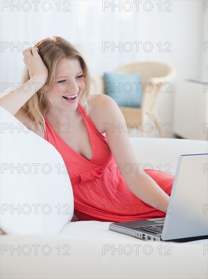 Young woman with laptop on sofa. Photo : Jamie Grill