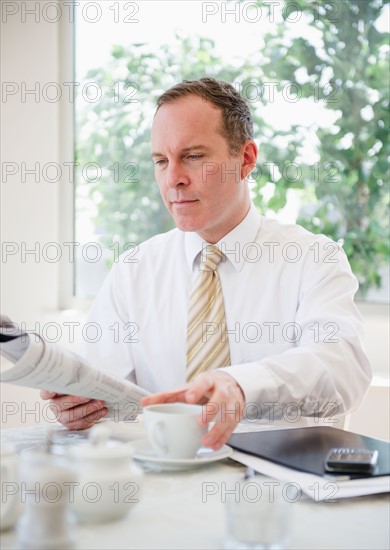 Businessman reading newspaper at table. Photo : Jamie Grill