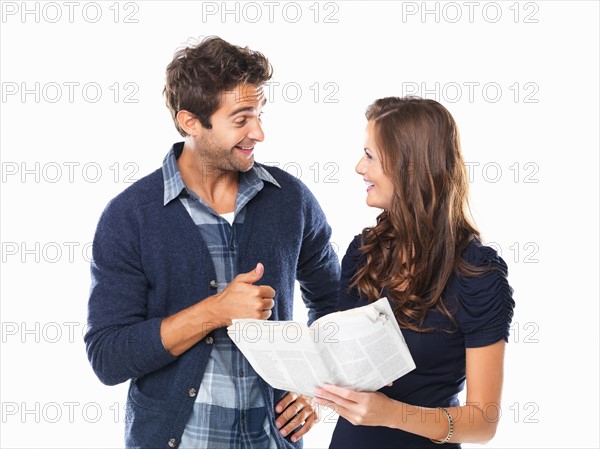 Studio shot of young couple with newspaper smiling and looking at each other. Photo : momentimages