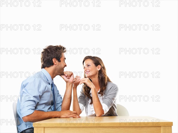 Business couple sitting at table with hands close to each other and smiling. Photo: momentimages