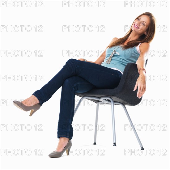 Studio shot of young woman sitting on chair and smiling. Photo : momentimages