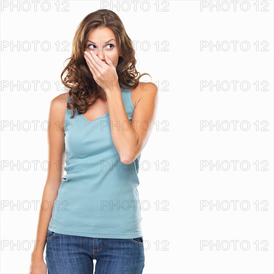 Studio shot of young woman with hand over mouth. Photo: momentimages