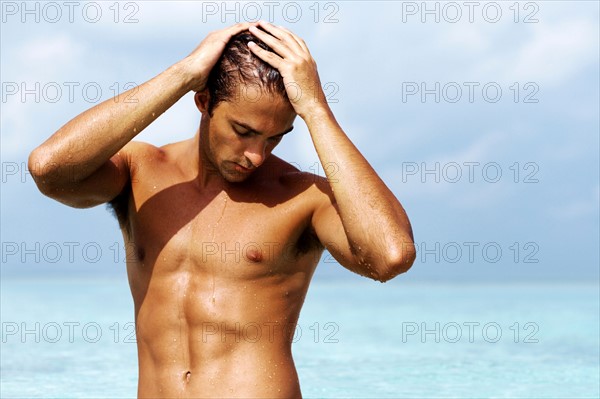 Handsome young guy standing in the sea. Photo : momentimages