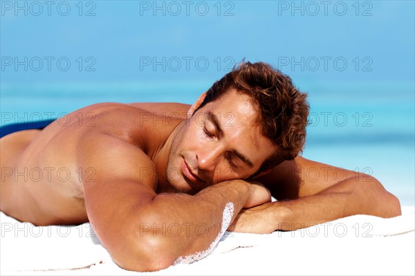 Handsome man taking sunbath at the beach. Photo: momentimages