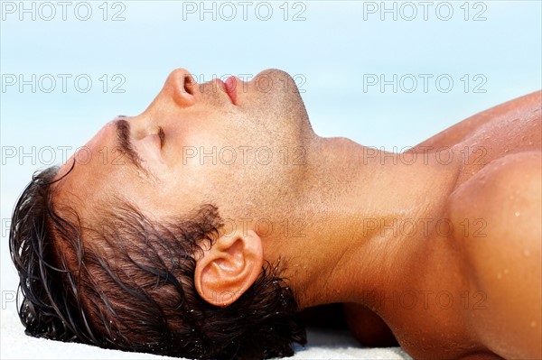 Profile of young guy lying on the beach. Photo: momentimages