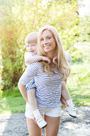 Young woman giving piggyback ride to son (2-3) in park. Photo : Take A Pix Media