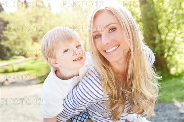Young woman giving piggyback ride to son (2-3) in park. Photo : Take A Pix Media