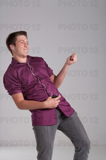 Portrait of smiling teenager playing air guitar, studio shot. Photo : Rob Lewine