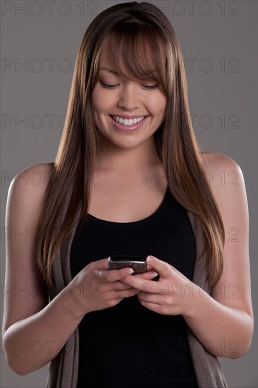 Portrait of young woman with mobile phone, studio shot. Photo : Rob Lewine