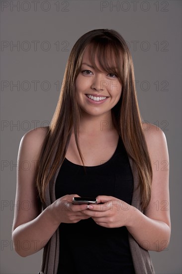 Portrait of young woman with mobile phone, studio shot. Photo : Rob Lewine