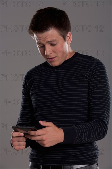 Portrait of teenage boy (16-17) with mobile phone, studio shot. Photo : Rob Lewine