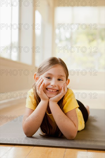 Girl (6-7) lying on exercising mat, smiling. Photo : Rob Lewine