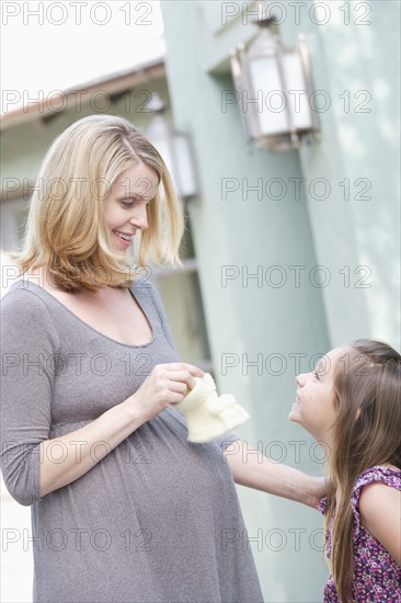 Pregnant mother holding baby booties standing with daughter (6-7) . Photo: Rob Lewine
