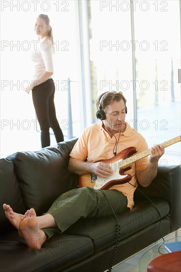 Mature man playing guitar woman standing next to window. Photo : Rob Lewine