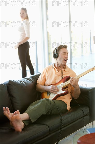 Mature man playing guitar woman standing next to window. Photo : Rob Lewine