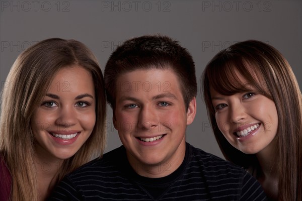 Portrait of teenage boy (16-17) and girl (16-17) with young friend, studio shot. Photo : Rob Lewine