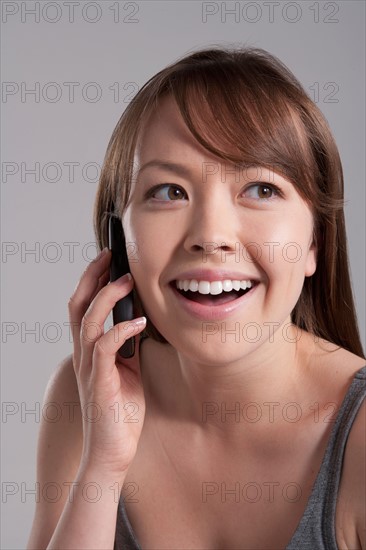 Portrait of young smiling woman using mobile phone, studio shot. Photo : Rob Lewine