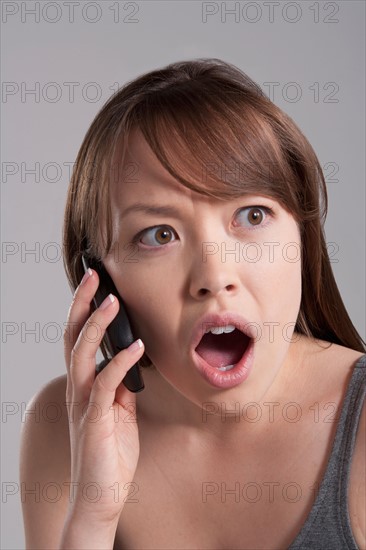 Portrait of young surprised woman using mobile phone, studio shot. Photo : Rob Lewine