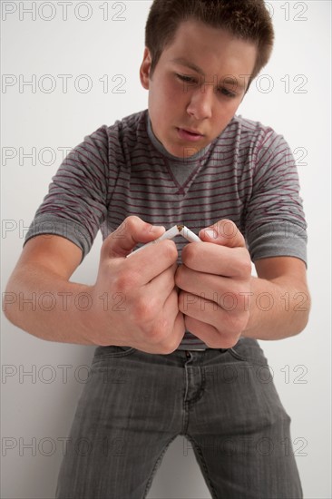 Teenage boy (16-17) breaking cigarette, studio shot. Photo : Rob Lewine