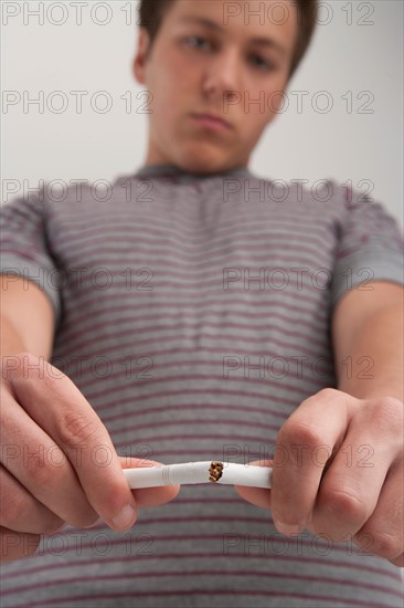 Teenage boy (16-17) breaking cigarette, studio shot. Photo : Rob Lewine