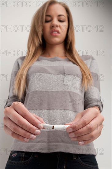 Teenage girl (16-17) breaking cigarette, studio shot. Photo : Rob Lewine